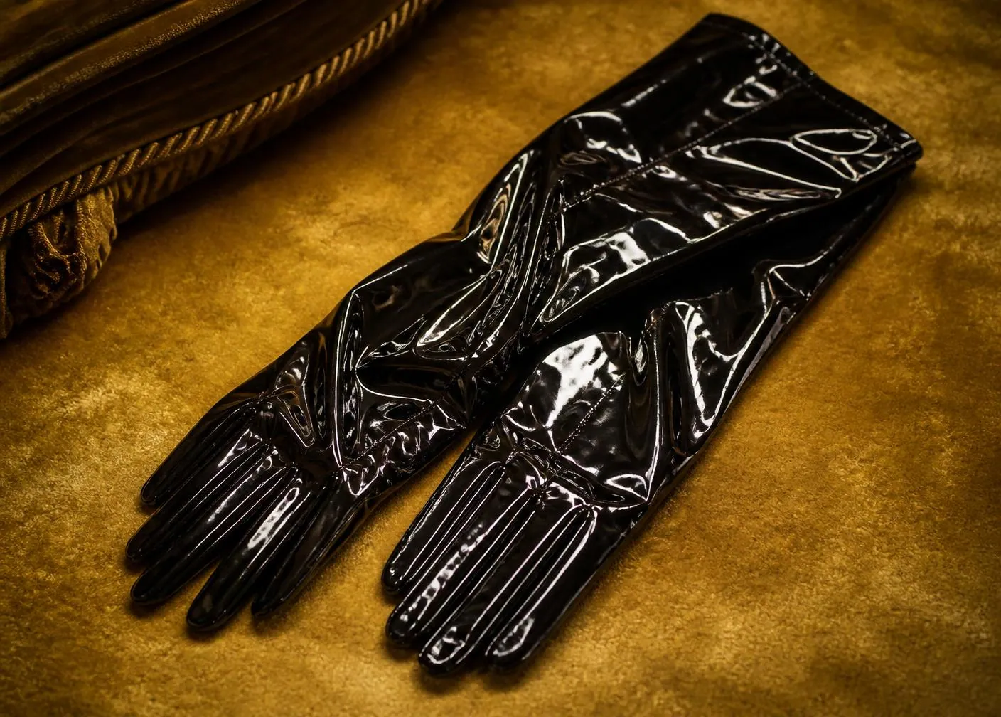 Schwarze Lackhandschuhe auf goldenem Samt – Lack-Escort Deutschland